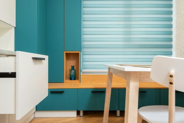 Open drawer against cabinet with vase on shelf and window blind in modern kitchen at home