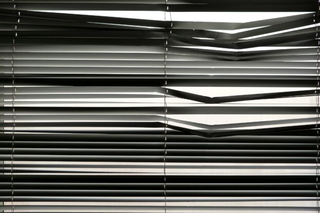 Horizontal venetian blinds creating a shadow pattern indoors with strong sunlight.