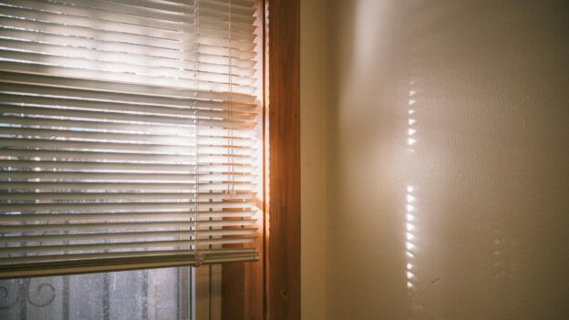 Warm sunlight casting shadows through window blinds, creating a tranquil indoor setting.
