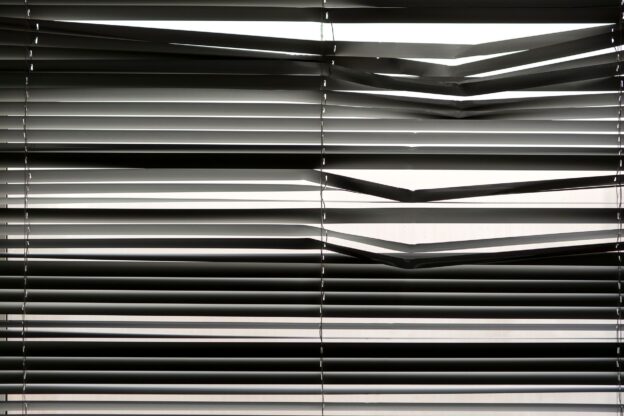 Horizontal venetian blinds creating a shadow pattern indoors with strong sunlight.